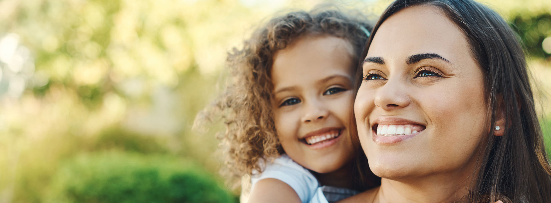 The image depicts a woman and a child, both smiling, embracing each other outdoors.