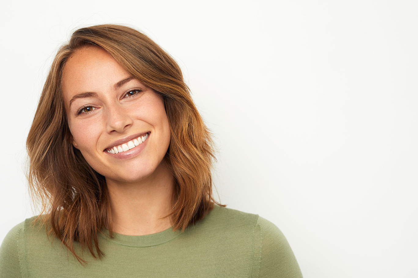 The image shows a woman with short hair, smiling at the camera. She is wearing a green top and has her hair styled in a bob cut.